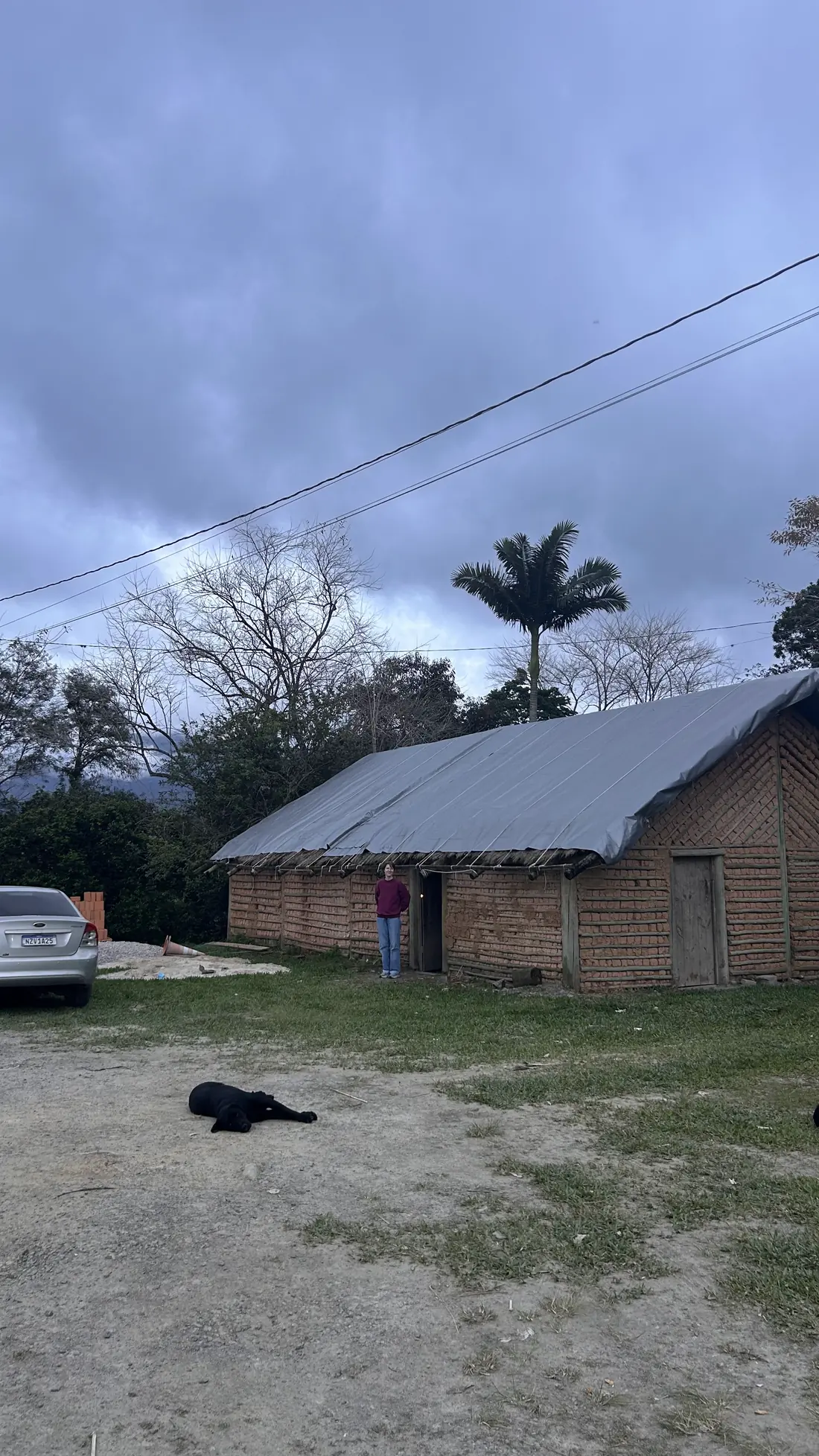 Construção de barro com telhado de lona ao entardecer, com uma palmeira ao fundo